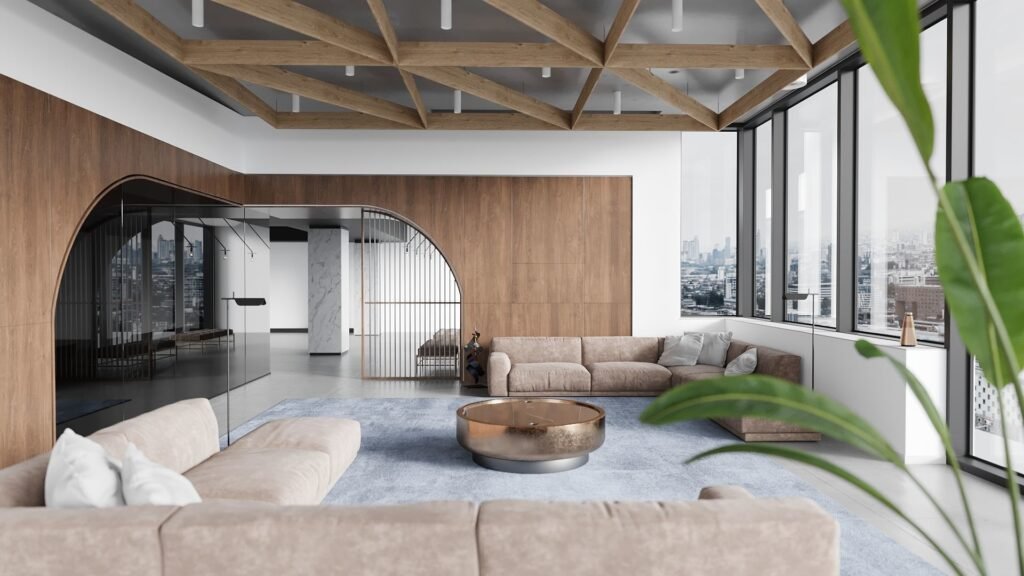 Spacious modern living room with floor-to-ceiling windows showcasing a panoramic city view. Features a light-colored sectional sofa with white pillows, a round metallic coffee table, and a textured light blue area rug.